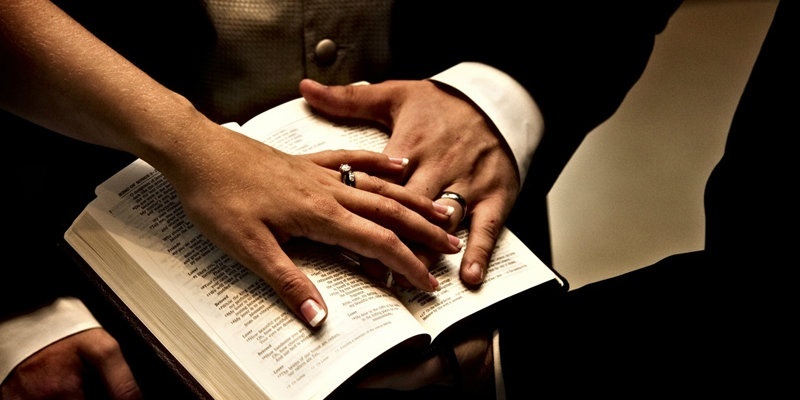 husband and wife with hands on opened bible